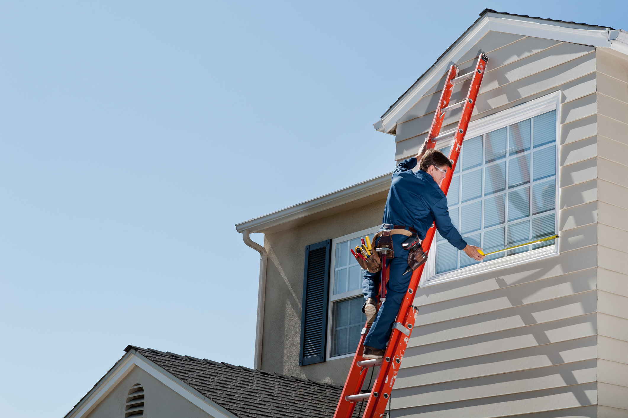 Professional window installer on ladder performing window replacement